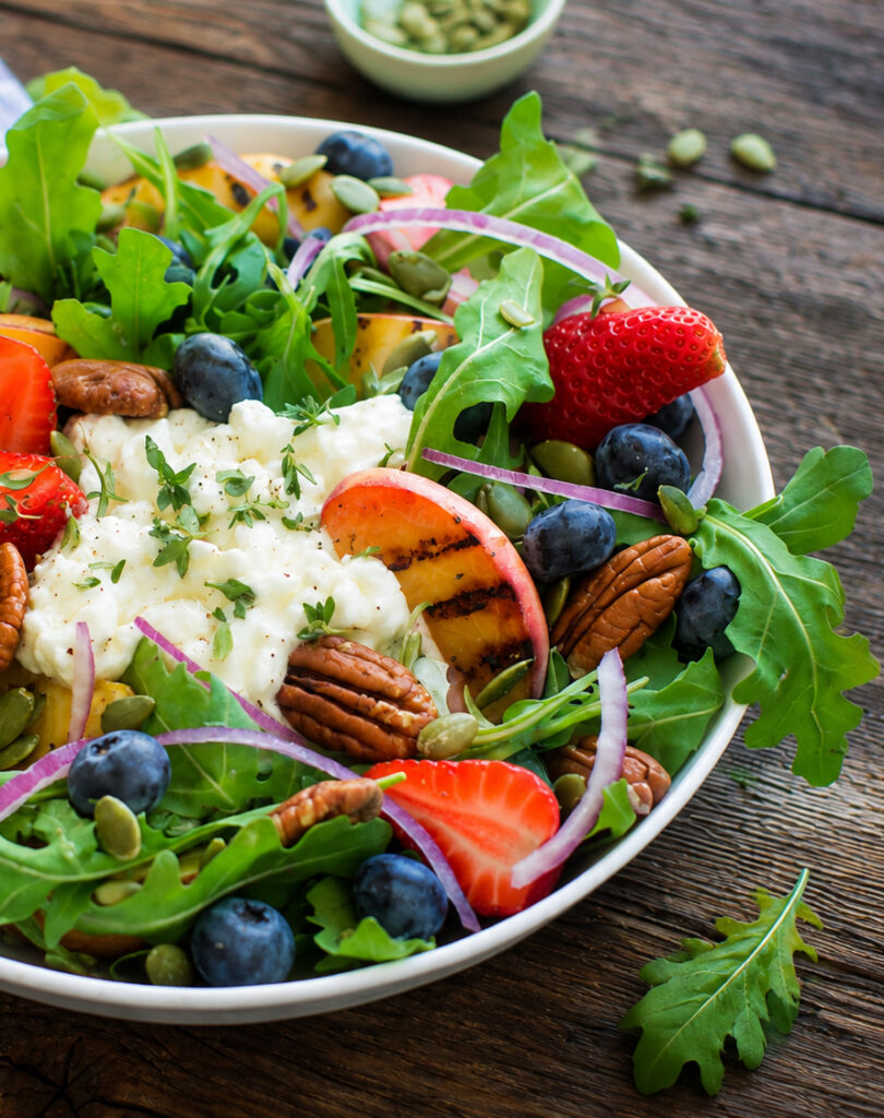 Salade de saison fraises, bleuets et cottage déposée dans un bol blanc, sur une planche de bois