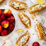 Sandwichs à hot-dog grillés aux crevettes nordiques, sauce crémeuse au citron et herbes, avec nectarine, prune sur un fond blanc et un bol de nectarines.