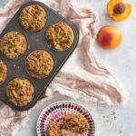 6 muffins aux pêches déposés dans un moule, accompagnée d'une pêche bien mûre