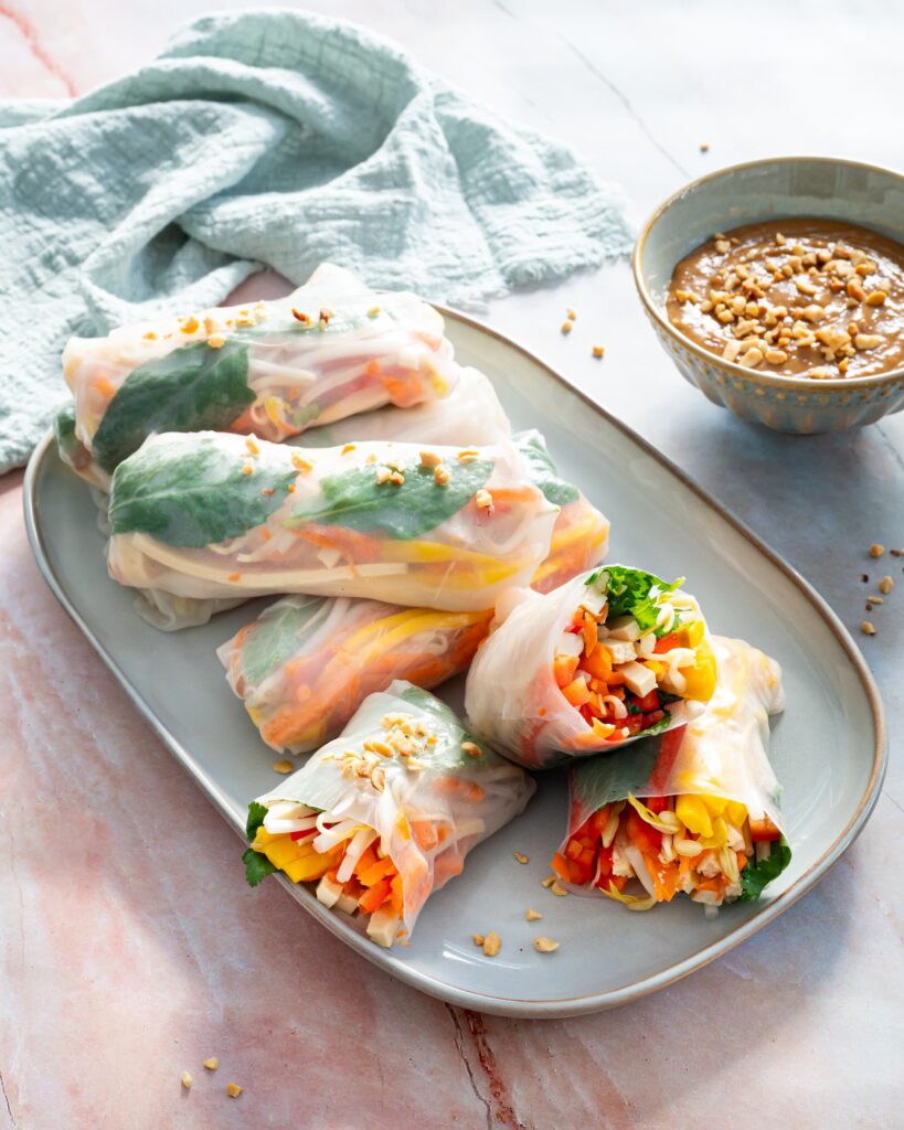 Rouleaux de printemps présentés dans une assiette grise et accompagnés d'une sauce à l'arachide