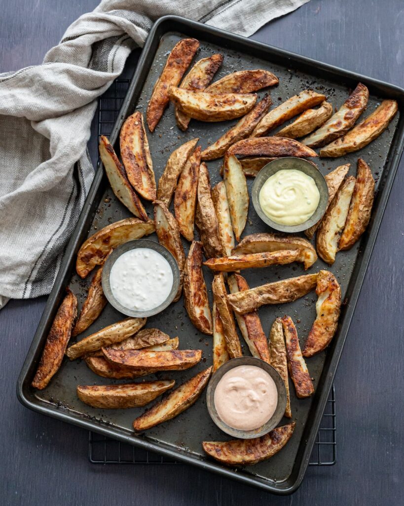 Frites cuites au four accompagnées de 3 sauces et déposées sur une plaque de cuisson