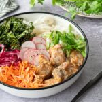 Bol blanc garni de saumon, de chou kale, de carottes râpées, de nouilles de riz et d'oignons rouges marinés