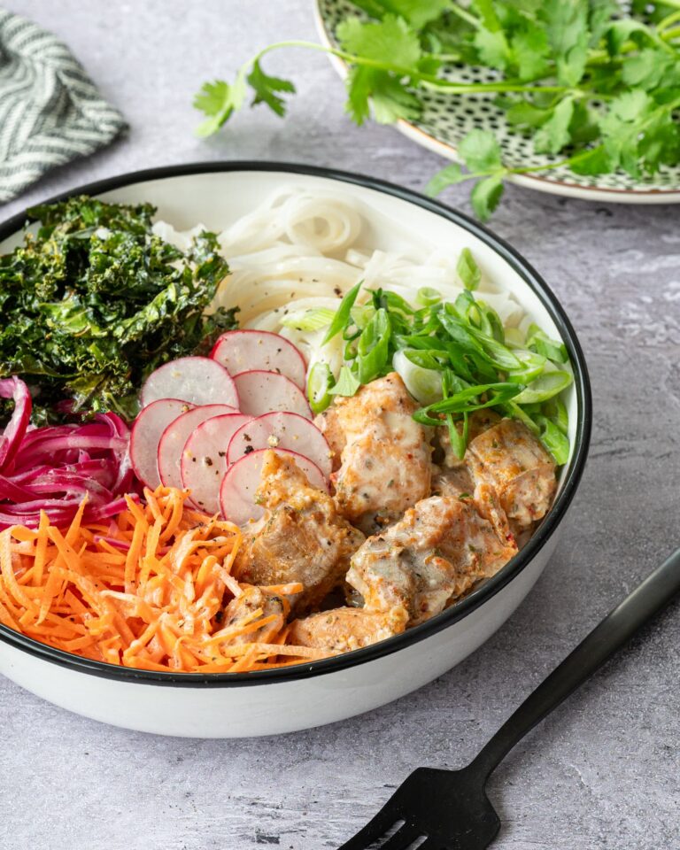 Bol blanc garni de saumon, de chou kale, de carottes râpées, de nouilles de riz et d'oignons rouges marinés