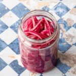 Pot d'oignons rouges émincés et marinés, déposé sur un fond bleu et beige quadrillé