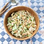 Salade de pâtes et saumon, fenouil, concombre et petits pois dans un bol en bois déposé sur un fond en losange bleu et blanc.