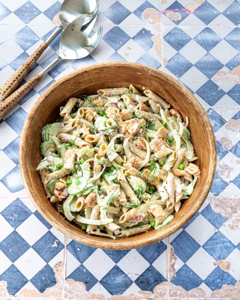 Salade de pâtes et saumon, fenouil, concombre et petits pois dans un bol en bois déposé sur un fond en losange bleu et blanc.