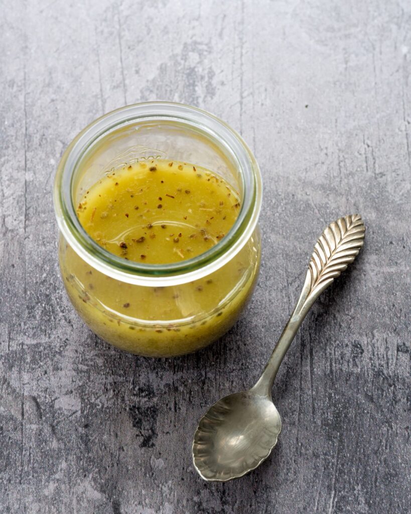 Vinaigrette polyvalente à l'huile d'avocat déposé dans un petit pot en vitre sur un fond gris