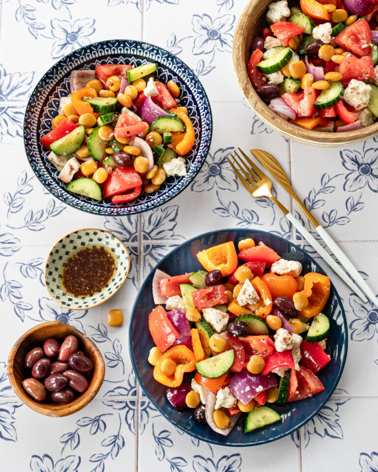 Salade grecque servie dans des assiettes bleues, accompagnées d'olives et de vinaigrette