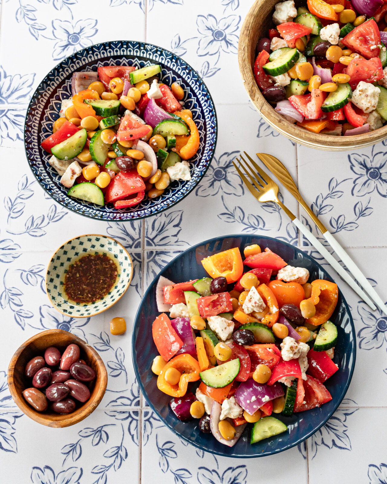 Salade grecque servie dans des assiettes bleues, accompagnées d'olives et de vinaigrette