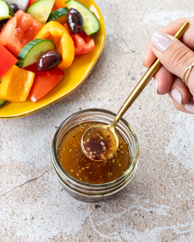 Vinaigrette grecque dans un petit pot transparent avec une cuillère dorée