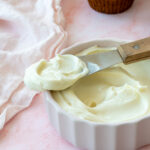 Un délicieux glaçage au chocolat blanc, fromage à la crème, yogourt et citron. Le tout déposer dans un bol blanc sur un fond rose pâle.