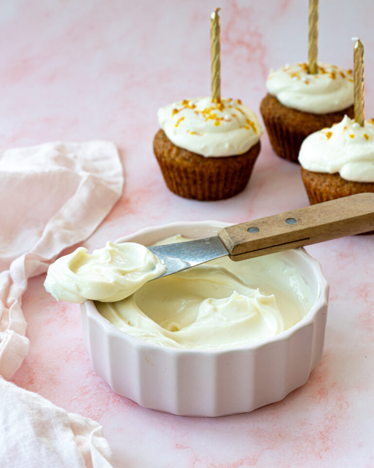 Un délicieux glaçage au chocolat blanc, fromage à la crème, yogourt et citron. Le tout déposer dans un bol blanc sur un fond rose pâle.