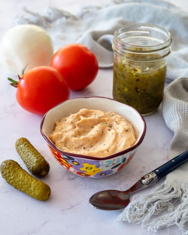 Sauce de style Big Mac déposée dans un petit bol coloré et accompagnée d'une tomate, de deux cornichons et de relish