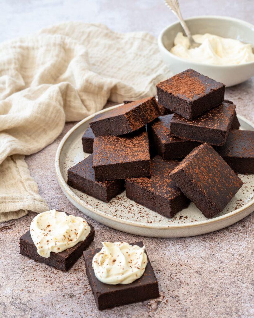 Décadent gâteau de style brownies coupés en carrés, déposés dans une assiette et saupoudrés de cacao