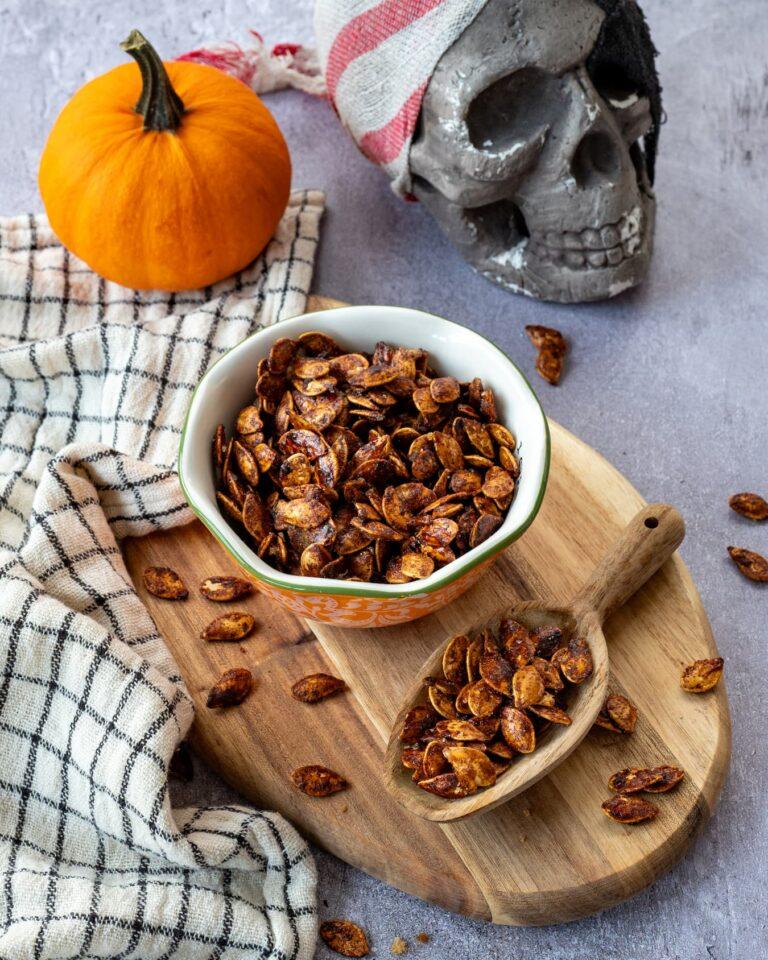 Graines de citrouille sucrées aux épices chaï déposées dans un petit bol accompagnées d'une petite citrouille et d'une tête de mort