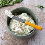 Fromage à la crème fouetté au romarin présenté dans un petit bol vert et accompagné d'une branche de romarin frais