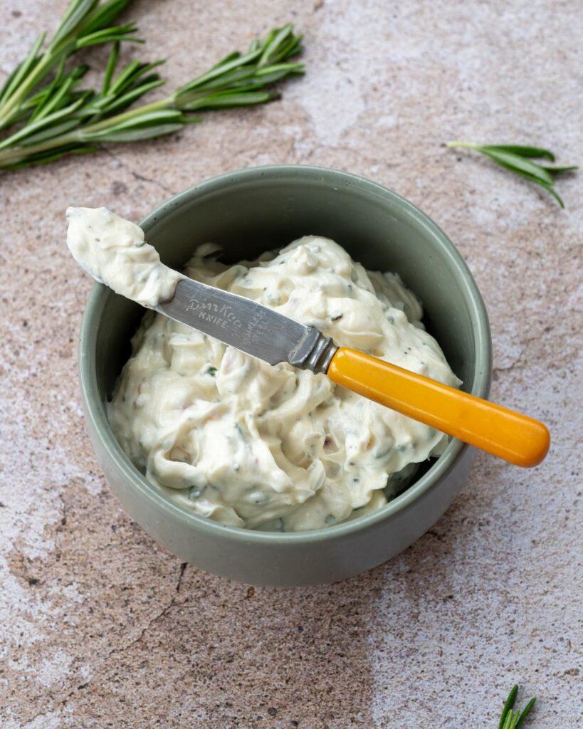 Fromage à la crème fouetté au romarin présenté dans un petit bol vert et accompagné d'une branche de romarin frais