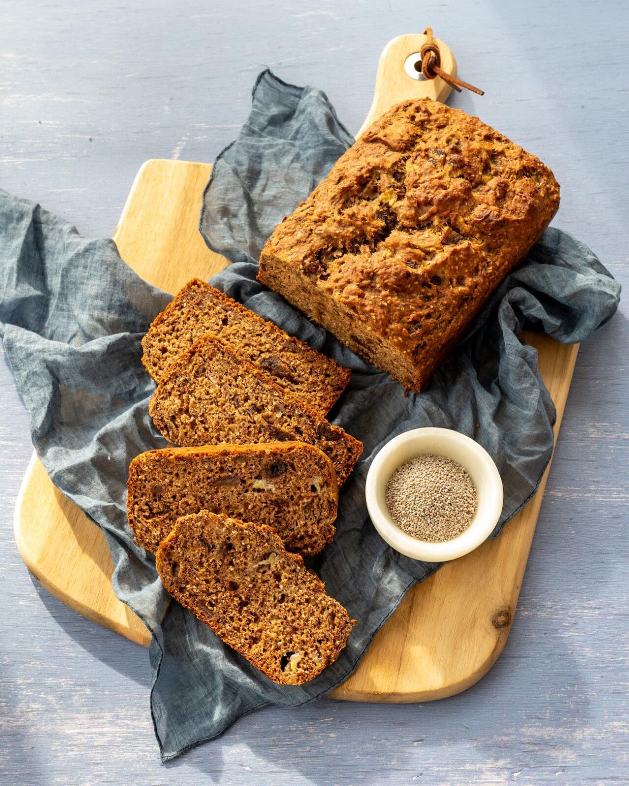 Pain aux bananes déposé sur une planche de bois, accompagné d'un linge bleu et de graines de chia