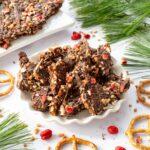 Bouchées de chocolat, bretzels et arachides sucrées déposées dans une assiette et accompagnées de branches de sapin en décoration