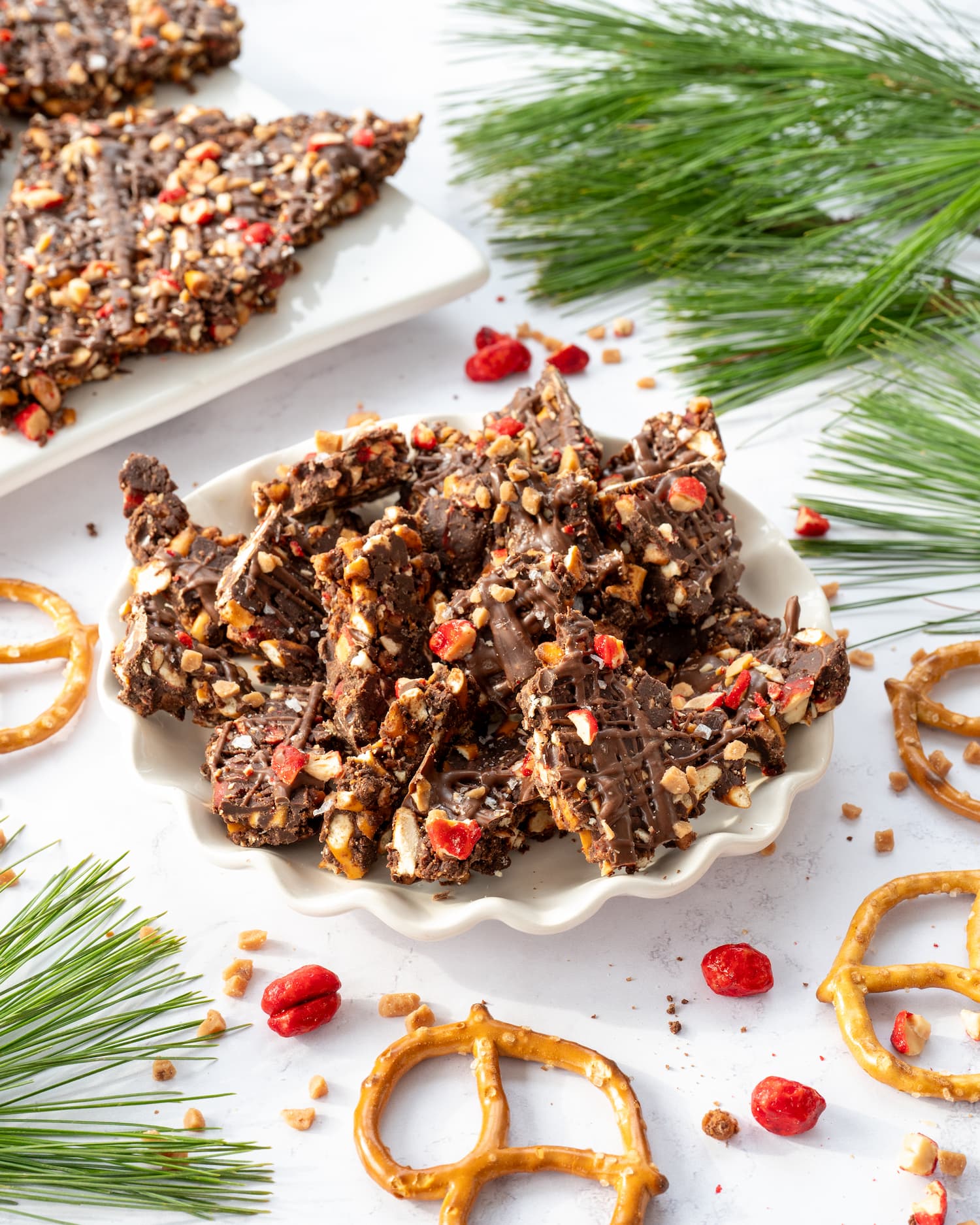 Bouchées de chocolat, bretzels et arachides sucrées déposées dans une assiette et accompagnées de branches de sapin en décoration