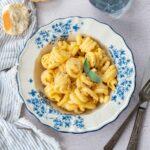 Trottole à la sauce crémeuse courge et sauge déposés dans une assiette blanche avec des fleurs bleues et accompagner d'un bout de pain