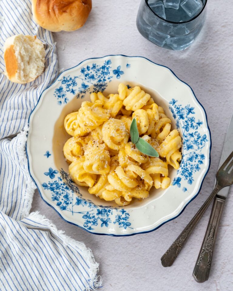 Trottole à la sauce crémeuse courge et sauge déposés dans une assiette blanche avec des fleurs bleues et accompagner d'un bout de pain