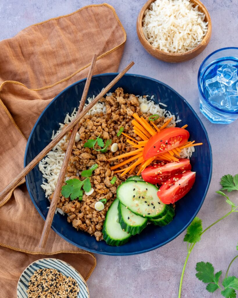 Boeuf haché aux épices asiatiques déposé dans u bol bleu et accompagné de riz, concombre et tomates