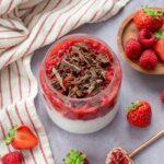 Petit contenant en verre rempli de pouding de chia et couvert d'une purée de framboises et fraises, ainsi que de chocolat râpé