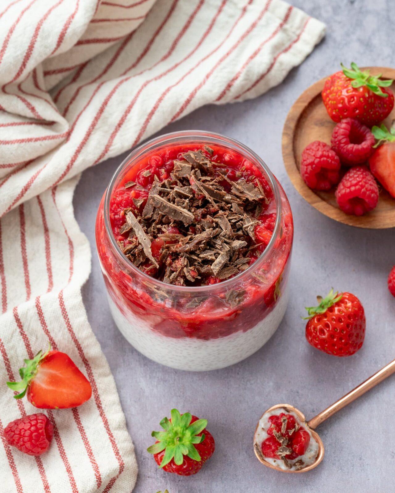 Petit contenant en verre rempli de pouding de chia et couvert d'une purée de framboises et fraises, ainsi que de chocolat râpé