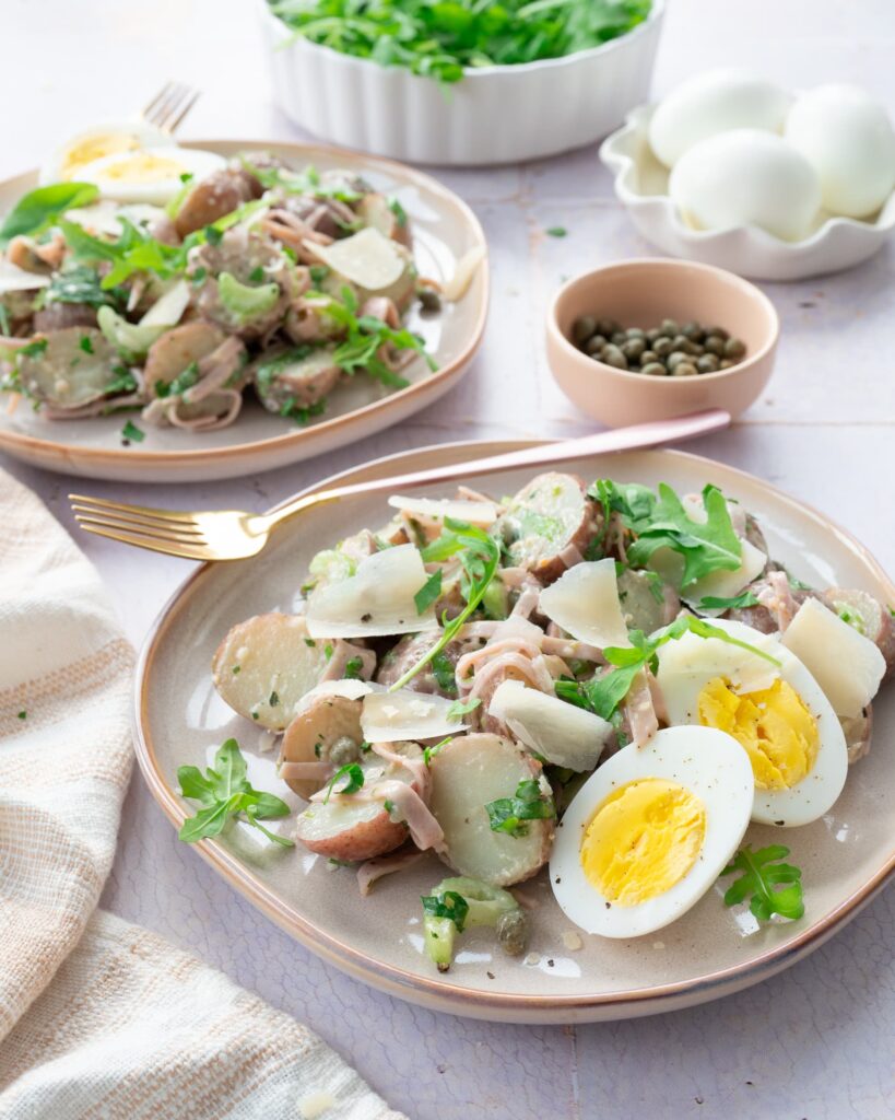 Salade de petites pommes de terre rouges accompagnées de jambon, d'un peu et de roquette, le tout déposé dans une assiette
