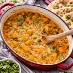 Mijoté de pois chiches à l'indienne servi dans une cocotte rouge et accompagné de riz, de pain naan et de coriandre