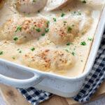 Moule rectangulaire blanc, dans lequel est déposé des poitrines de poulet dans une sauce blanche et parsemés de paprika et persil frais