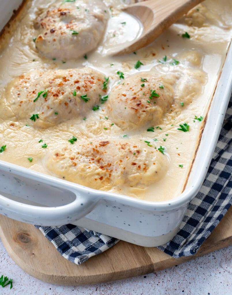 Moule rectangulaire blanc, dans lequel est déposé des poitrines de poulet dans une sauce blanche et parsemés de paprika et persil frais