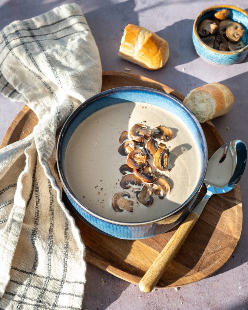 Crème de champignons déposée dans un bol bleu, et garnit de champignons tranchés et poêlés