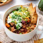 Chili à la PVT servi dans un bol blanc, et garni de yogourt grec, de guacamole et de chips de tortillas