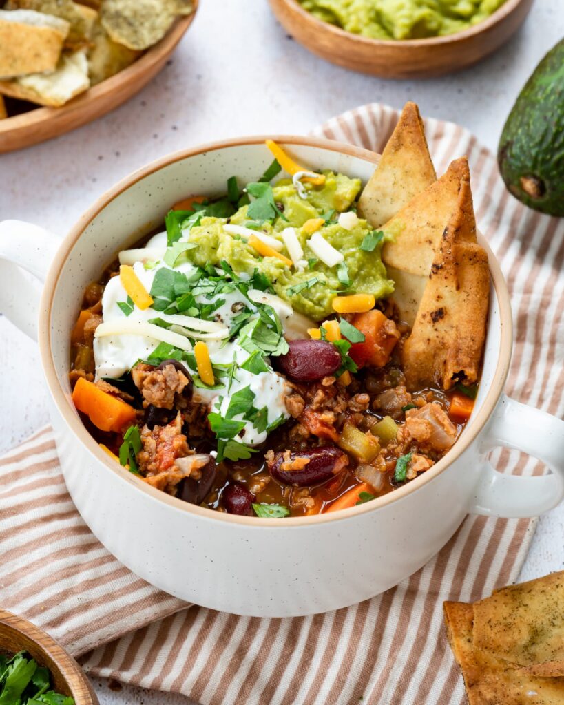 Chili à la PVT servi dans un bol blanc, et garni de yogourt grec, de guacamole et de chips de tortillas