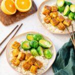 Cubes de tofu à l'orange accompagnés de riz et de choux de Bruxelles déposés dans une assiette beige