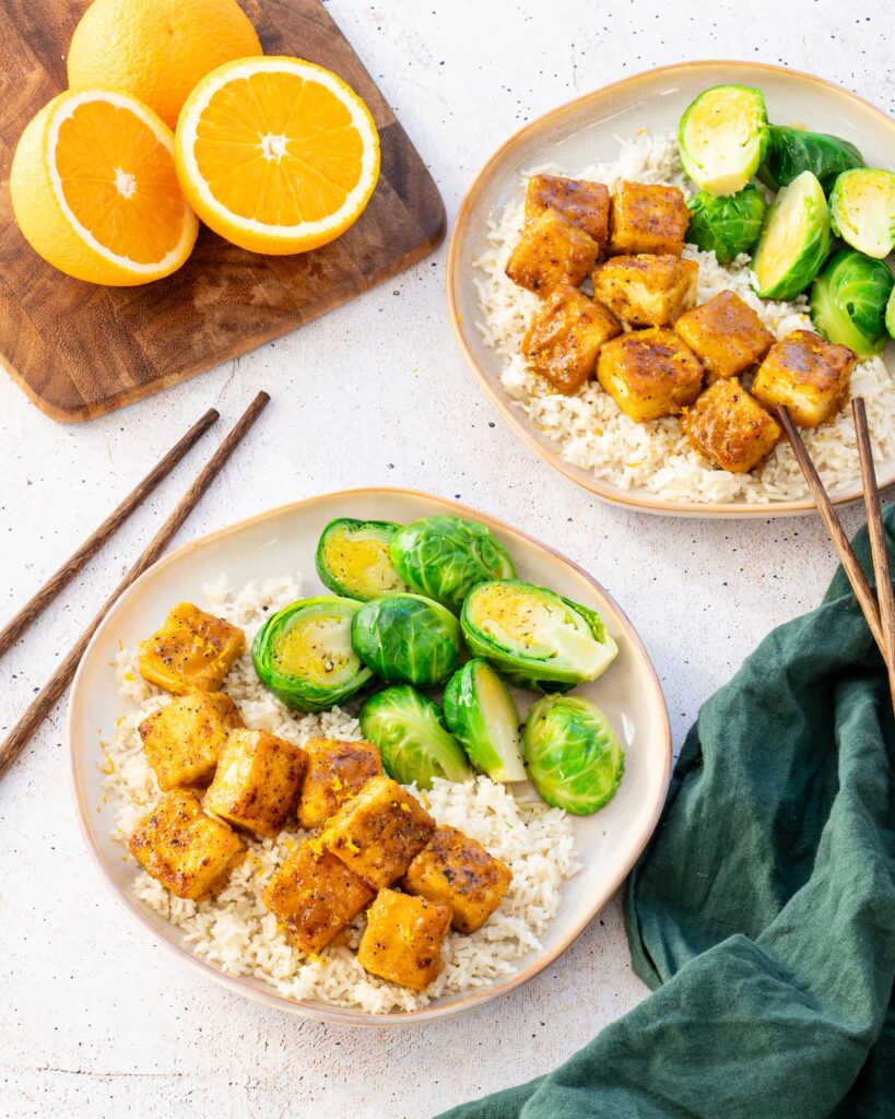 Cubes de tofu à l'orange accompagnés de riz et de choux de Bruxelles déposés dans une assiette beige