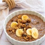 Gruau aux bananes, arachide et cacao dans un bol blanc et garnit de rondelles de banane et de granola