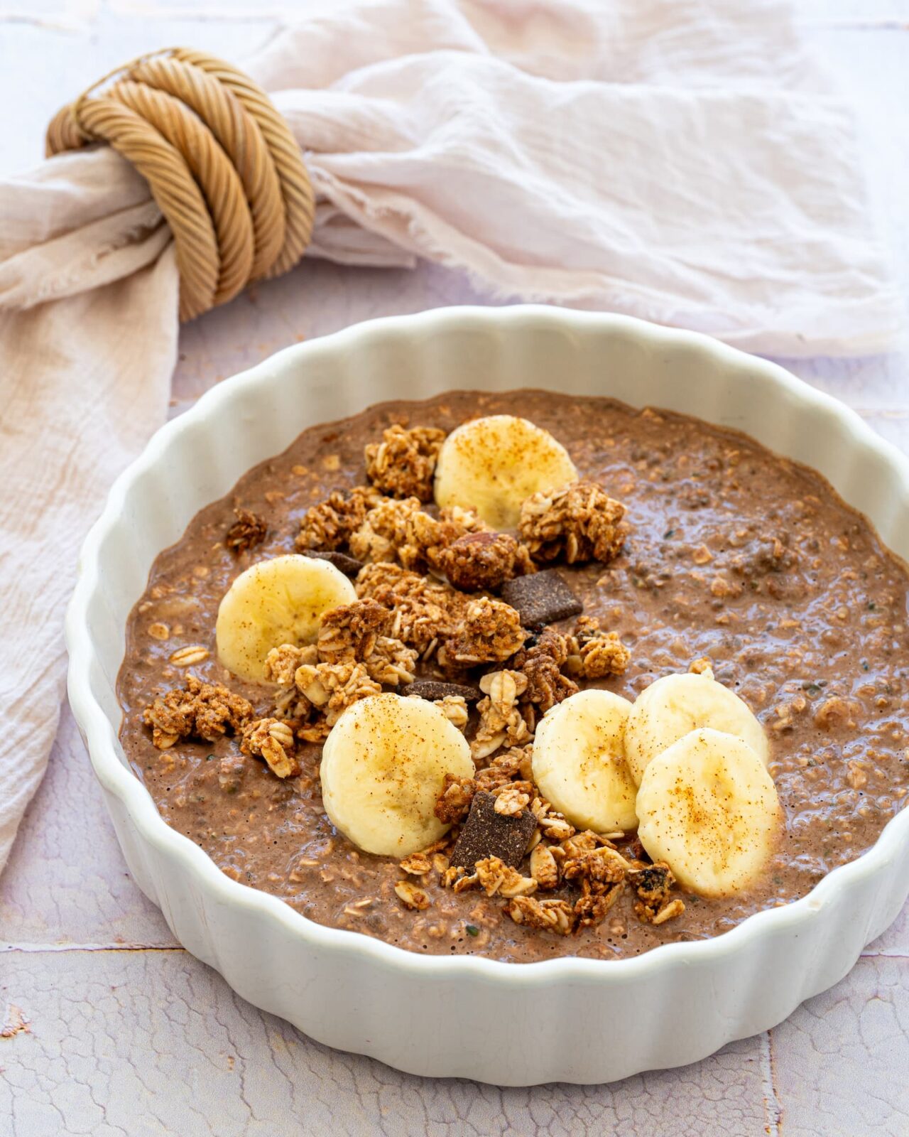 Gruau aux bananes, arachide et cacao dans un bol blanc et garnit de rondelles de banane et de granola