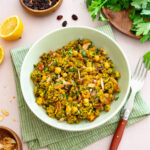 Casserole de quinoa et pois chiches à l'indienne déposée dans un bol vert et accompagnée de raisins secs, amandes et persil plat