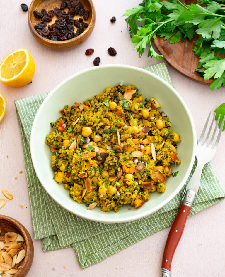 Casserole de quinoa et pois chiches à l'indienne déposée dans un bol vert et accompagnée de raisins secs, amandes et persil plat