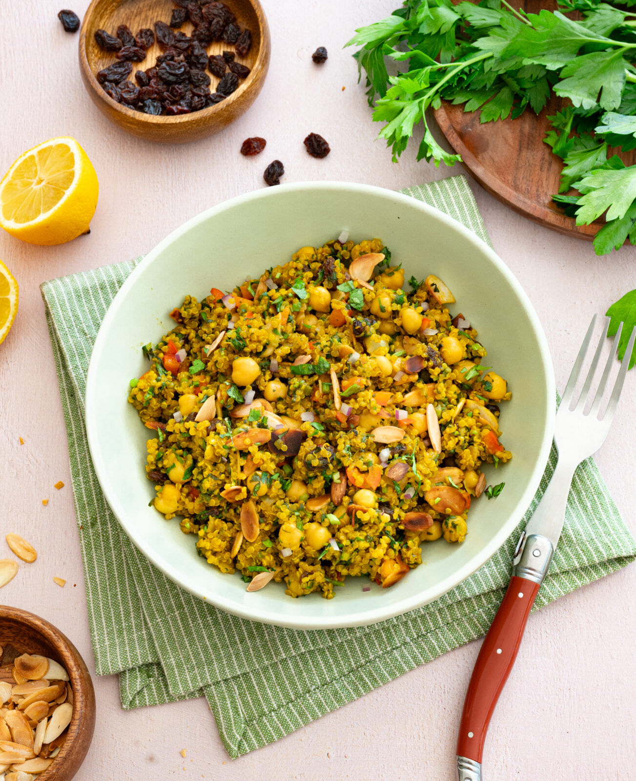 Casserole de quinoa et pois chiches à l'indienne déposée dans un bol vert et accompagnée de raisins secs, amandes et persil plat