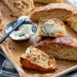 Scones au cheddar fort, ciboulette et thym déposés sur une plaque de cuisson et accompagnés de fromage à la crème