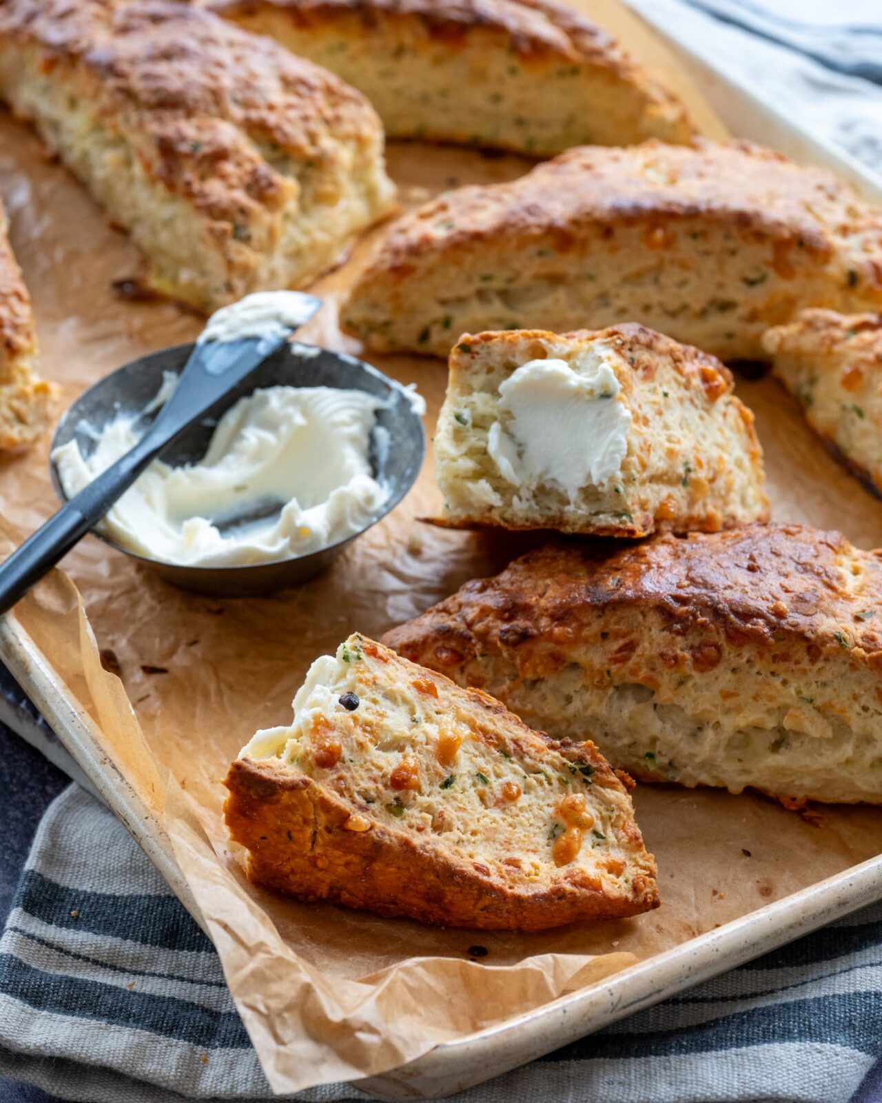 Scones au cheddar fort, ciboulette et thym déposés sur une plaque de cuisson et accompagnés de fromage à la crème